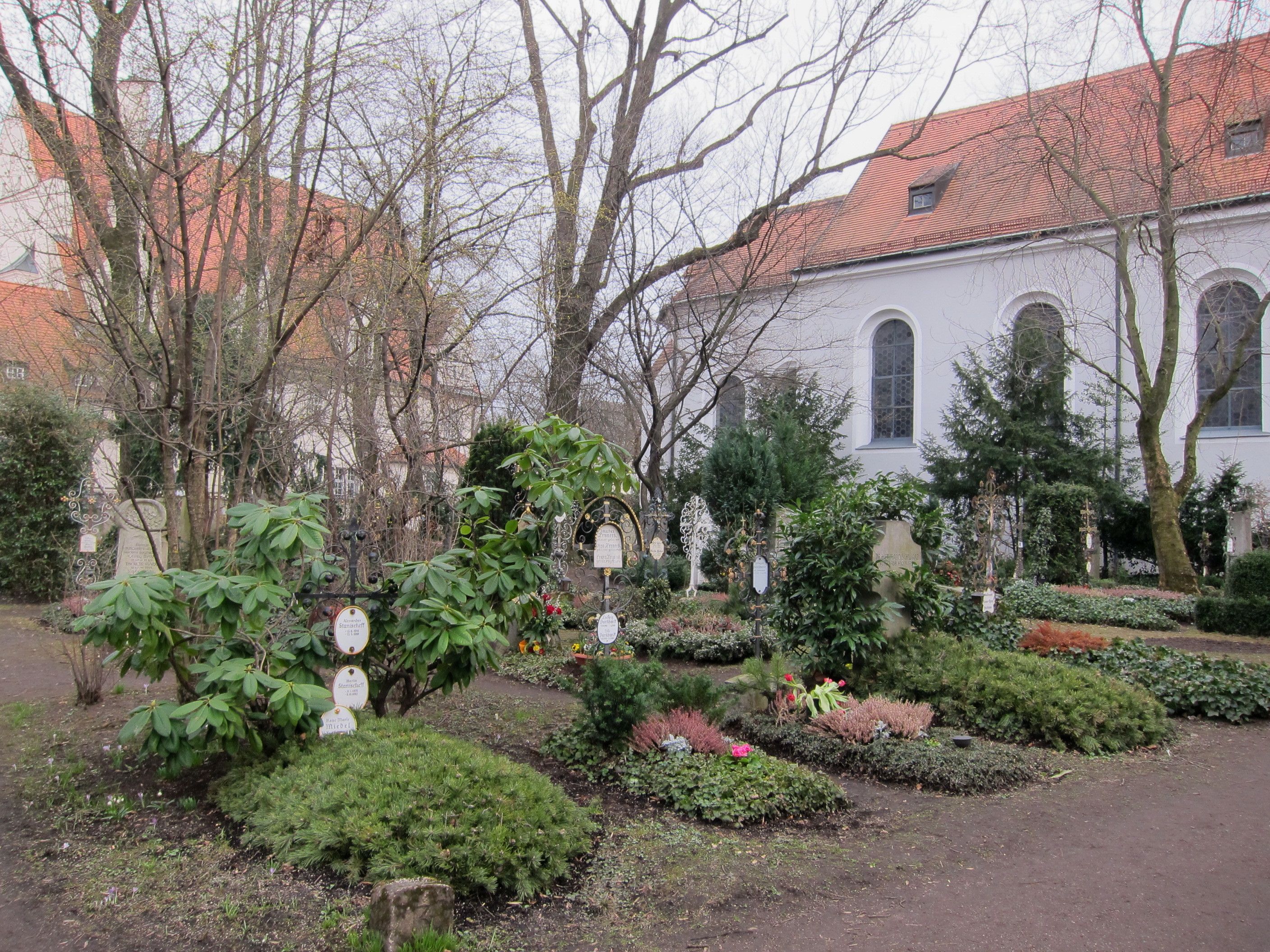 Kirche St. Georg hinter der Friedhofsmauer und Grabstätten des Friedhofs Bogenhausen